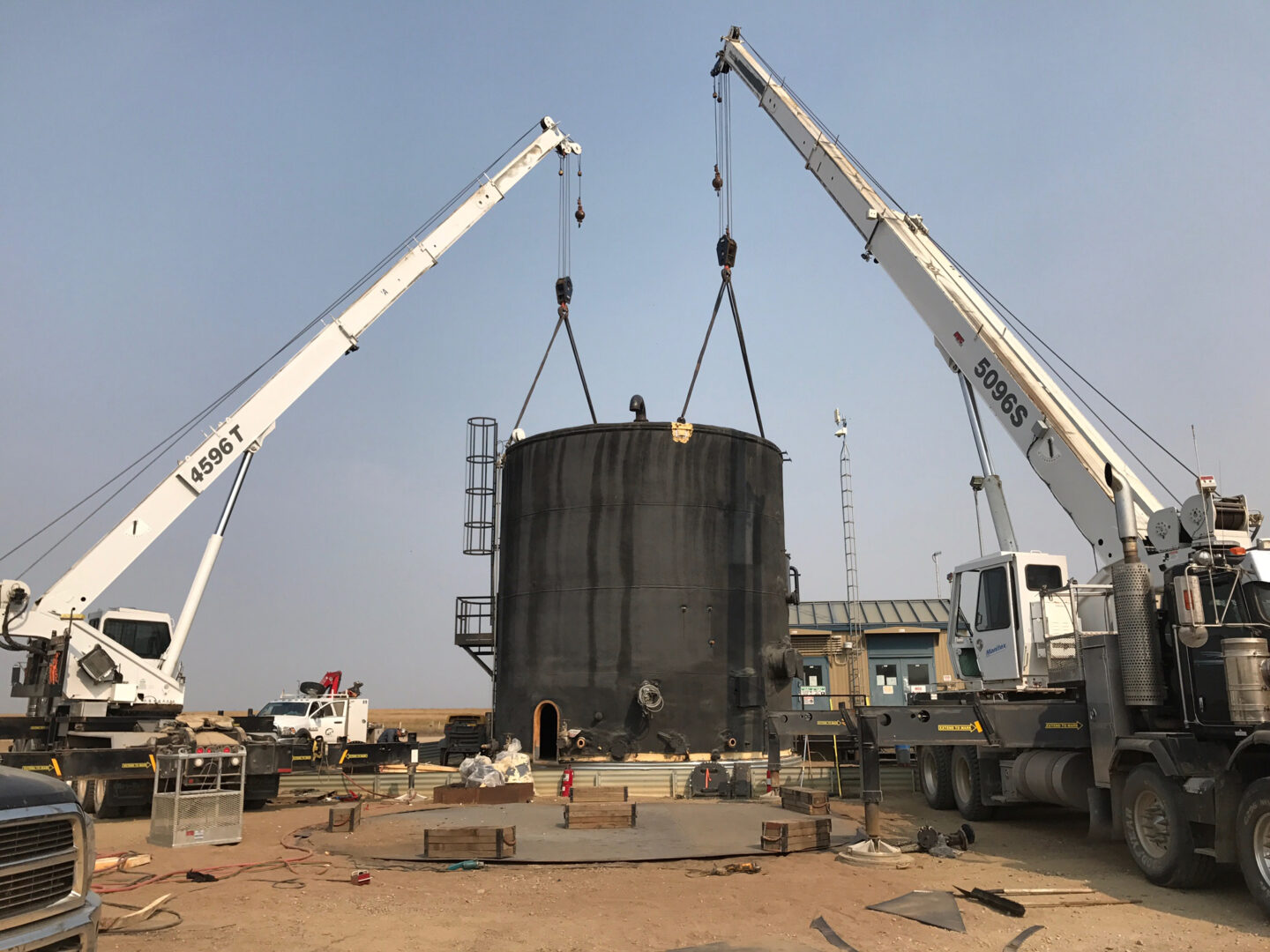 A large metal tank being lifted by two cranes.